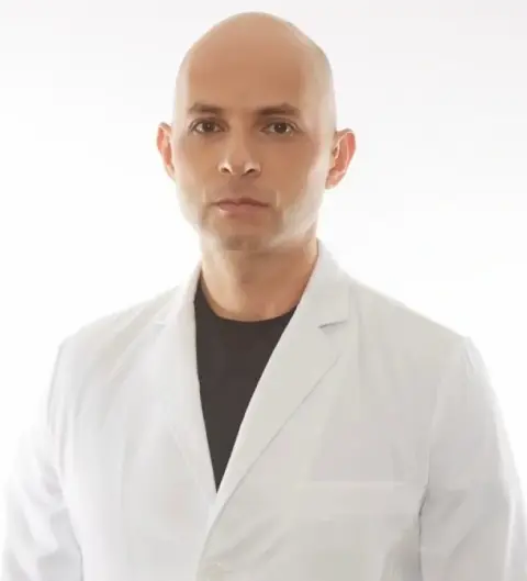A man in white lab coat and black shirt.